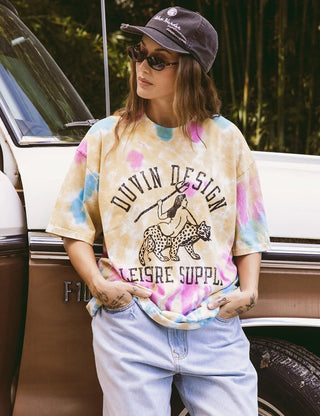 Model wearing the Duvin Leopard Tee in yellow, pink, and blue tie dye with a black leopard-and-rider graphic and Duvin Design Leisure Supply lettering
