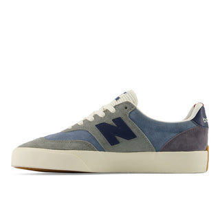 A New Balance low-top sneaker in a color-blocked palette of slate blue, gray suede, and navy, featuring a thick cream midsole and white laces, shown from a side profile on a white background.